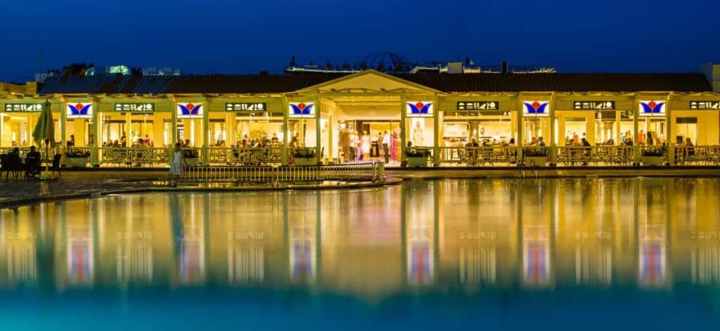 Brightly lit apartments along the water at night, showcasing inviting outdoor spaces and modern desi.