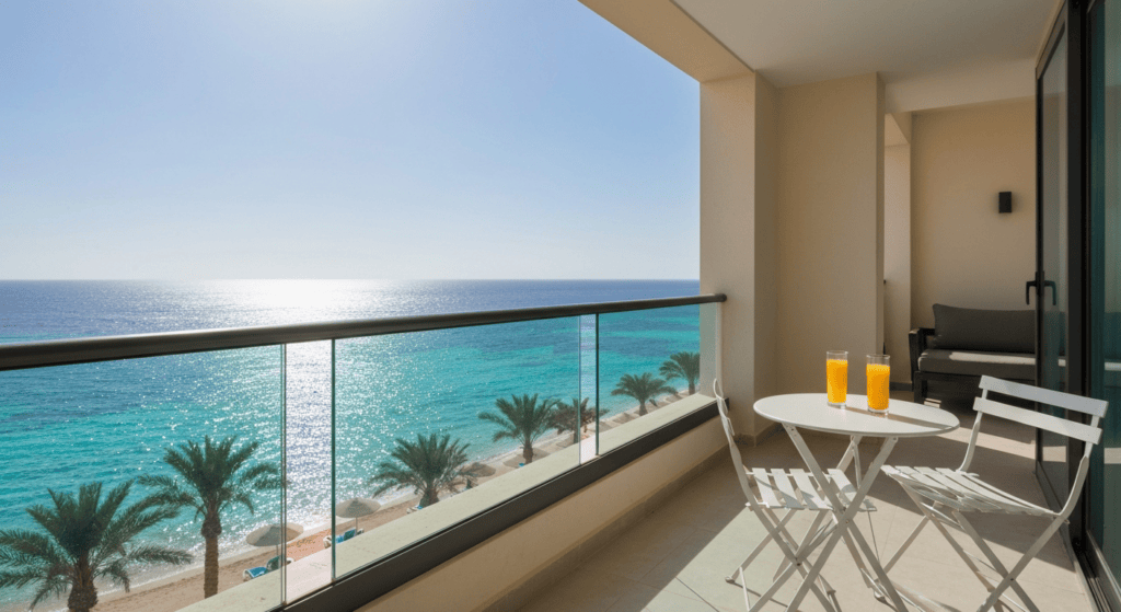 Balcony overlooking the turquoise sea with a small table and two glasses of orange juice.