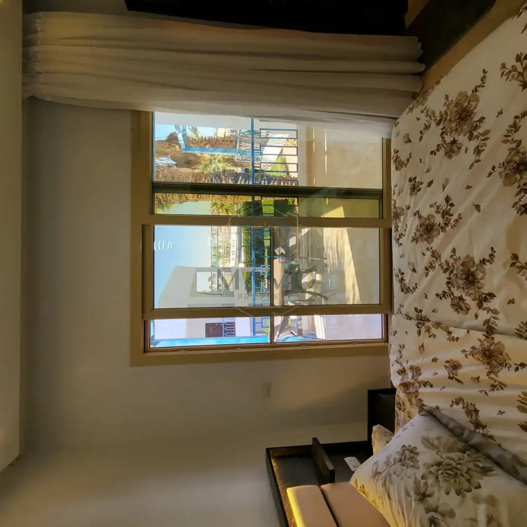 Bedroom with large window and balcony overlooking the city and sea.